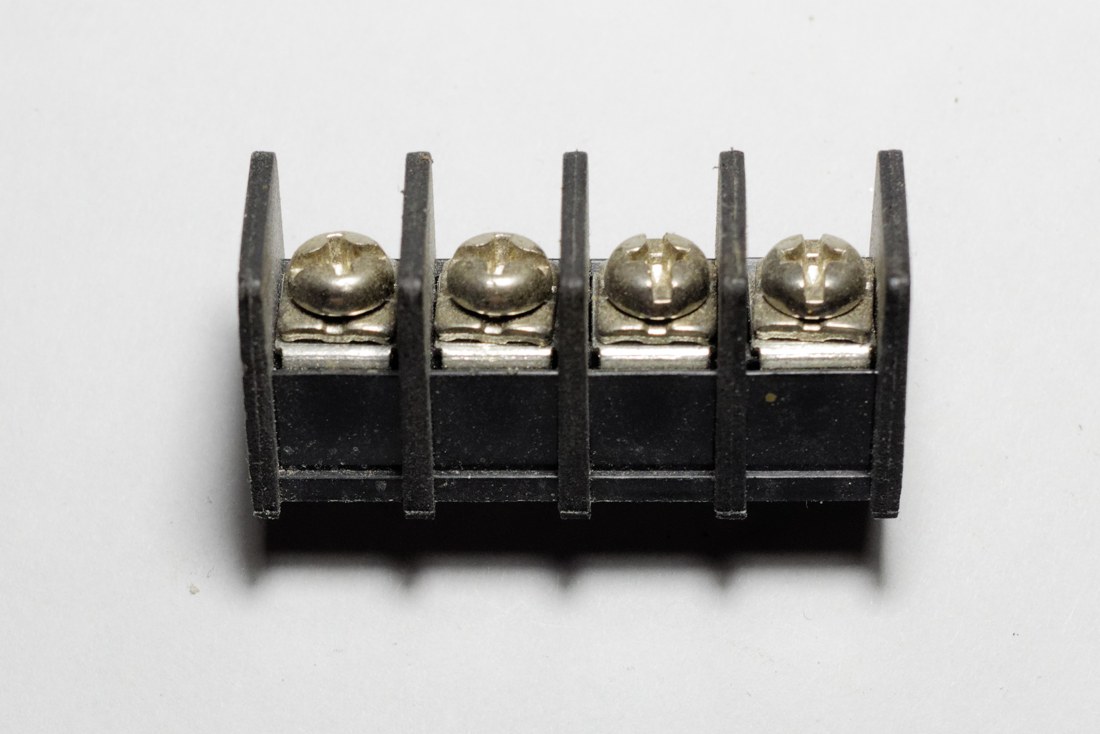 Bornier électrique noir à quatre bornes alignées et vis de serrage métalliques apparentes.