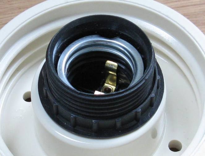 Intérieur d’une douille E27 blanche avec un filetage métallique et contact central en laiton visibles.