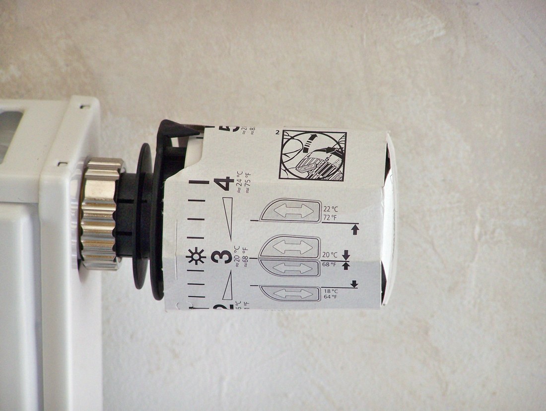 Tête thermostatique blanche graduée de radiateur, fixée latéralement sur une vanne dans une pièce.