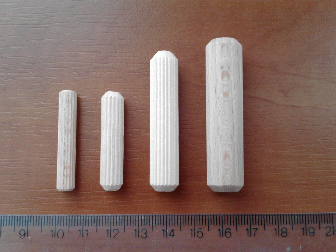 Quatre tourillons cylindriques en bois rainuré, de diamètres différents, à côté d’une règle graduée.