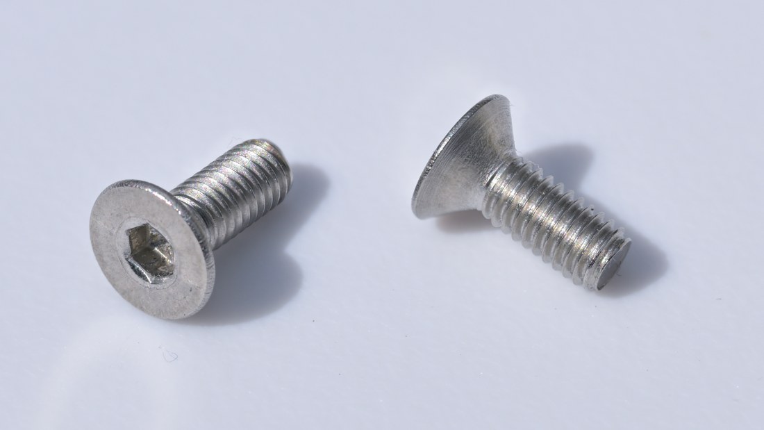Deux vis métalliques courtes à tête fraisée conique, dont une montre une empreinte six pans creux.